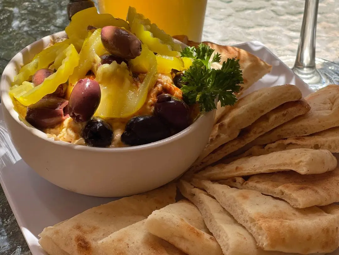 Meze hummus topped with paprika, olive oil, Kalamata olives and pepper rings with pita